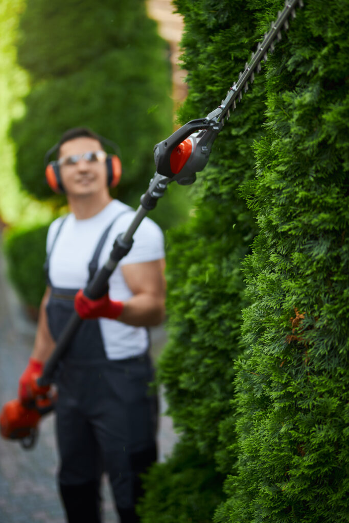 man in uniform trimming hedge during summer time